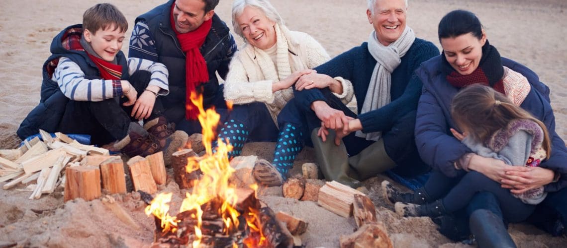 Multi Generation Family Sitting By Fire On Winter Beach