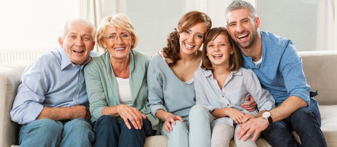 Grandparents, patents and cute girl sitting on sofa at home and laughing at camera